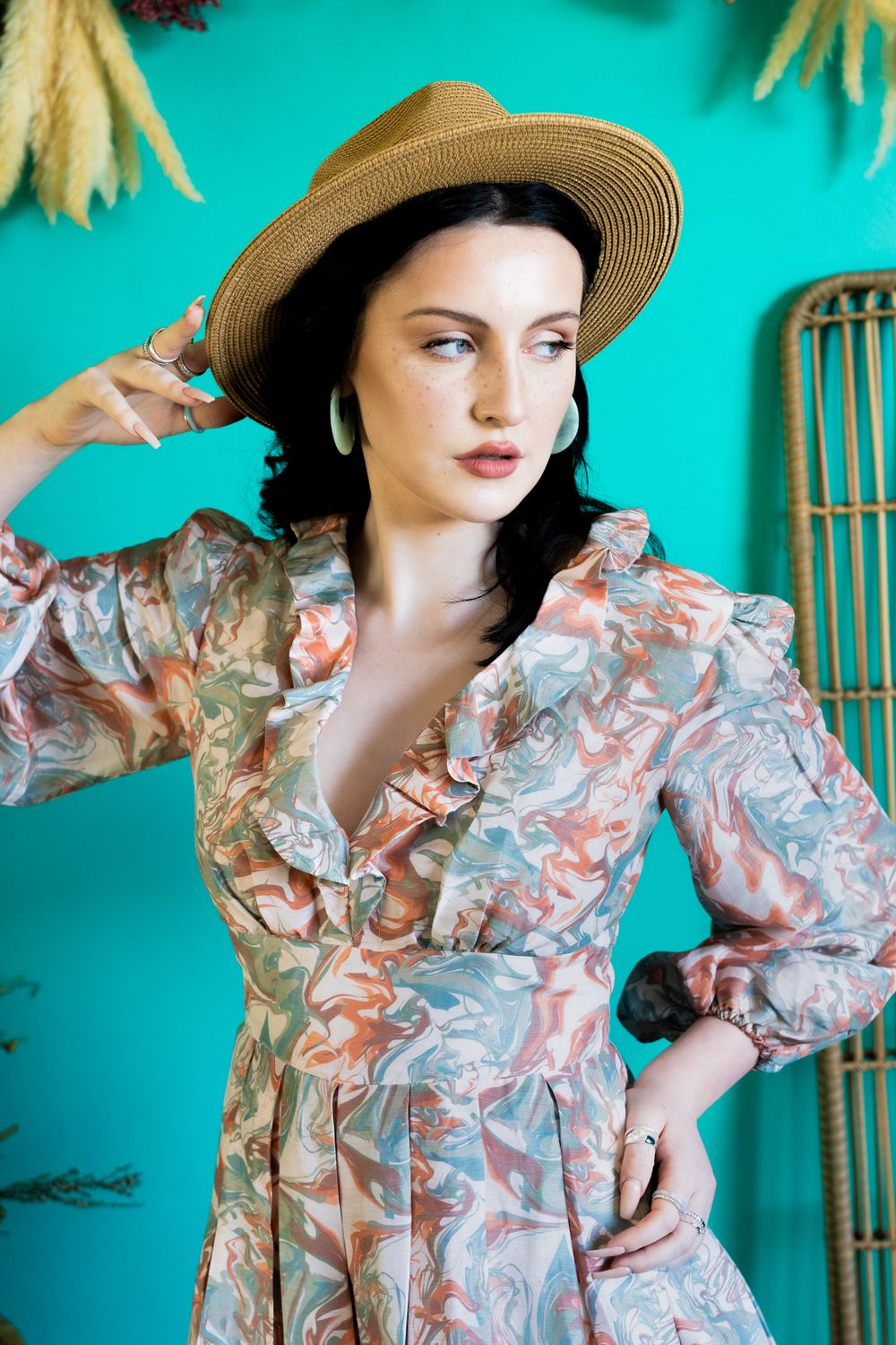 Fashion portrait with straw hat and floral dress against vibrant turquoise background.