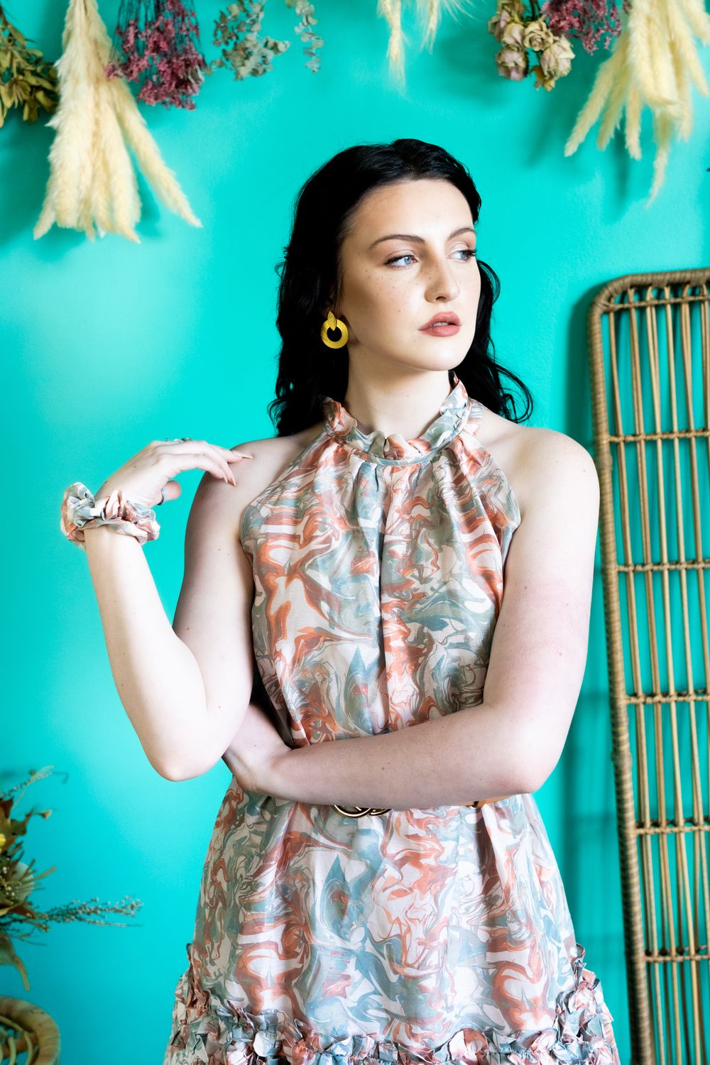 Elegant portrait with yellow earrings and floral halter dress against turquoise backdrop.