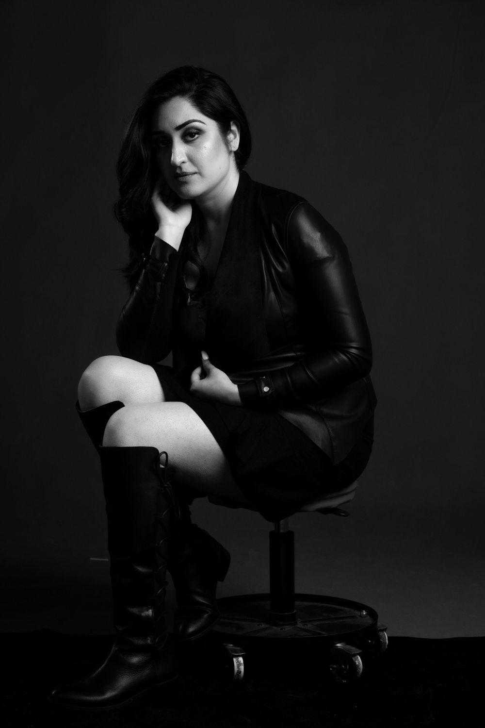 A dramatic black and white portrait against dark background features a model in leather jacket and tall boots.