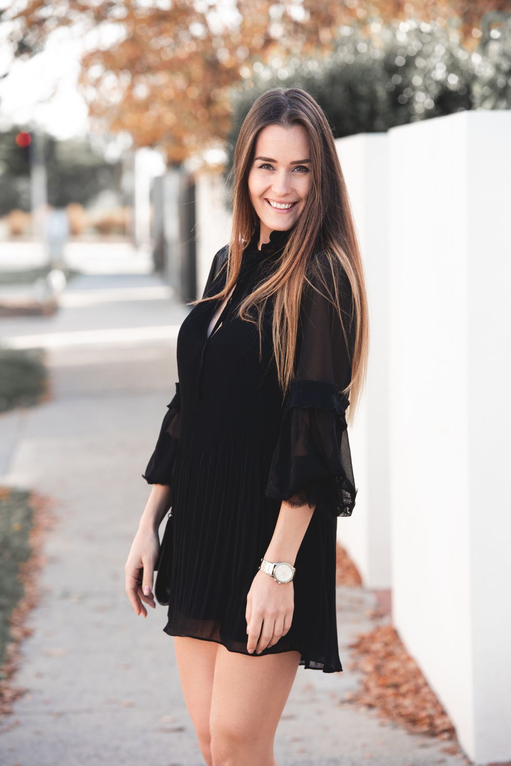 Woman in black dress poses on sidewalk during autumn.