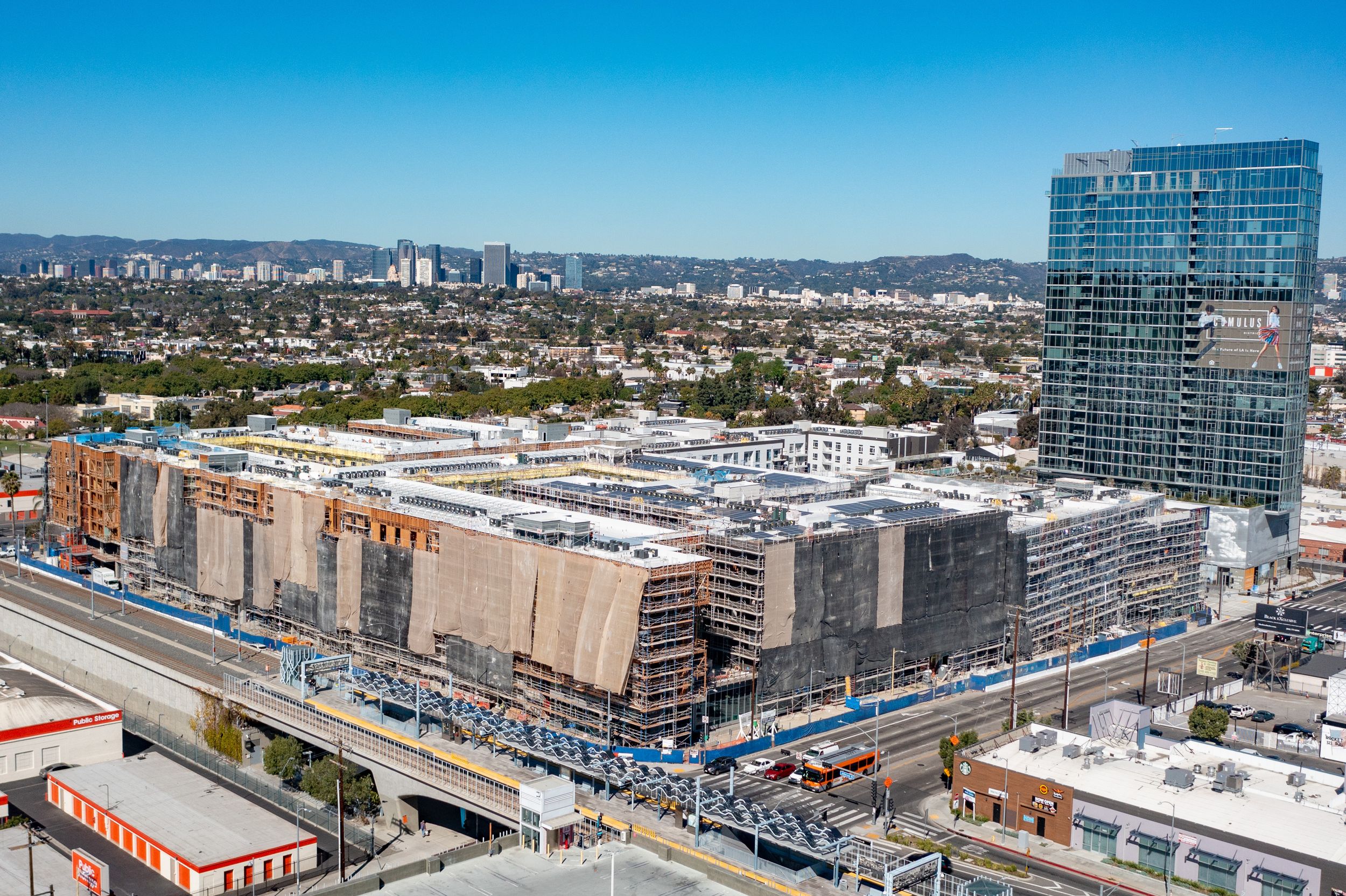 Aerial perspective of a major transit-oriented real estate development under construction alongside a busy light rail transit corridor and e
