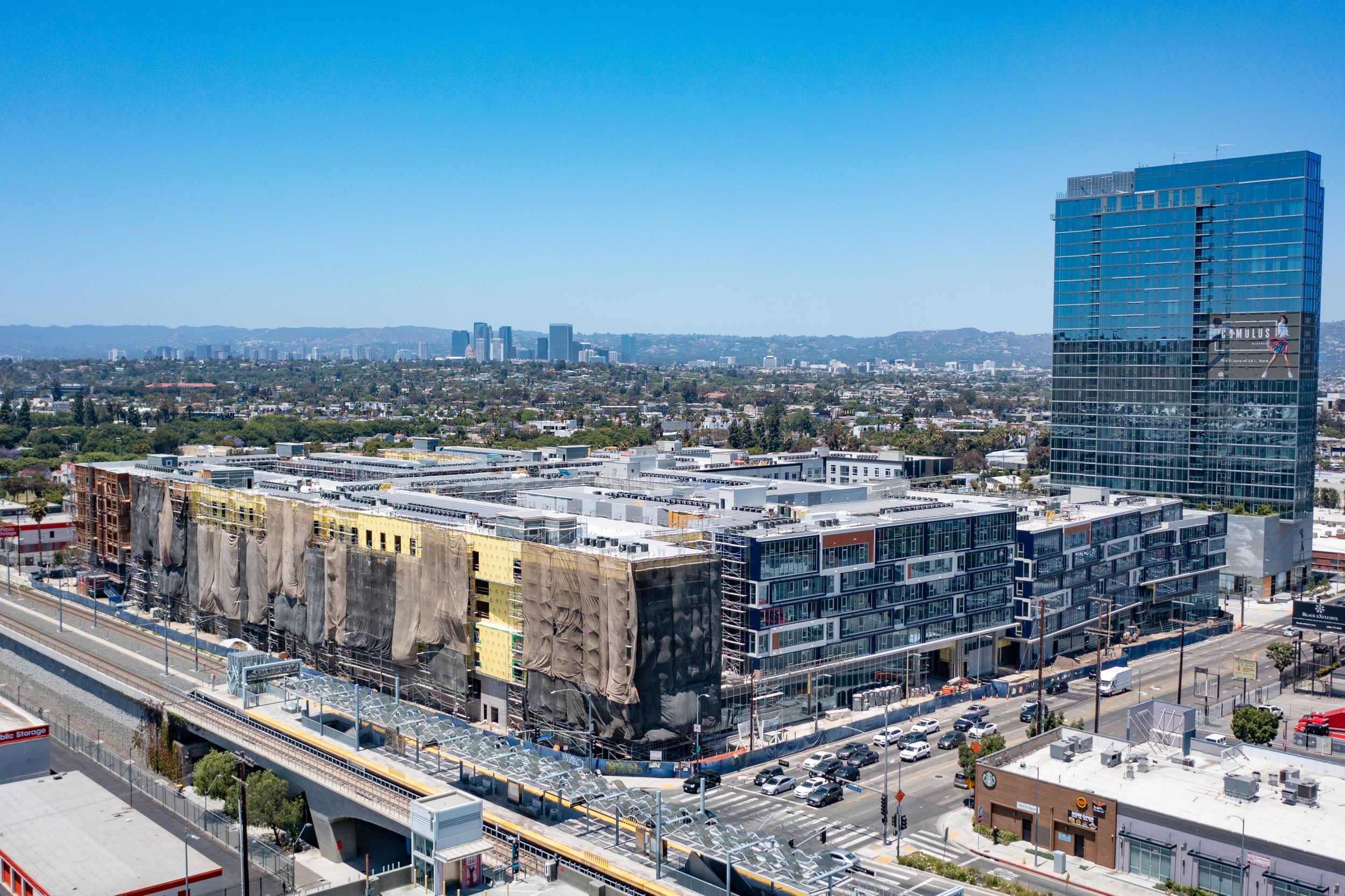 Aerial perspective of a large transit-oriented real estate development adjacent to a light rail station and established urban skyscrapers.