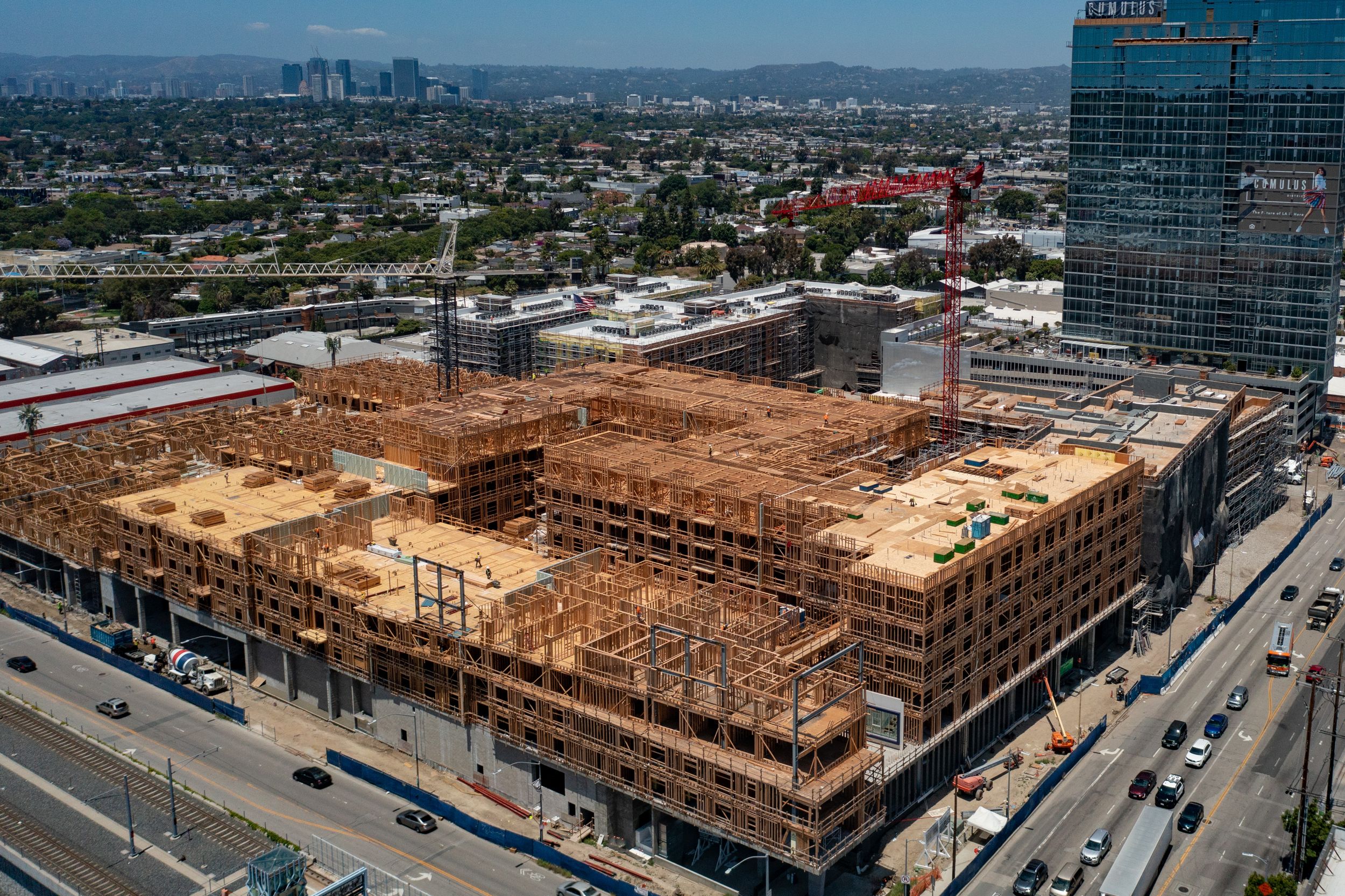 Aerial perspective of an expanding city skyline highlighting a large-scale, wood-framed residential building under construction near establi