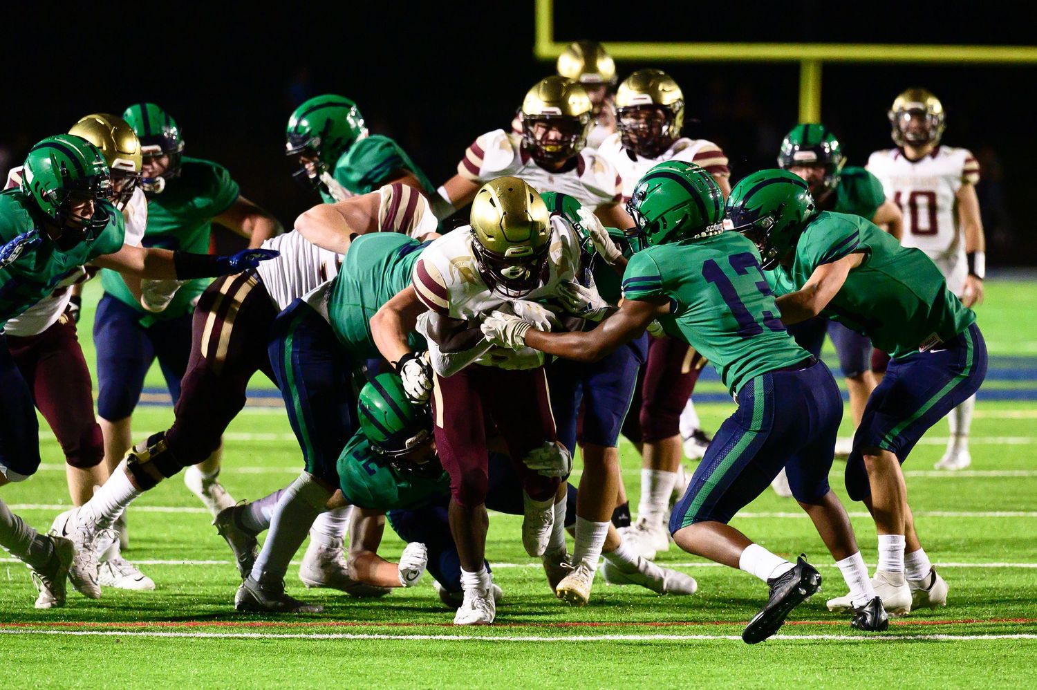 Football players in green and white jerseys clash during an intense nighttime game play.