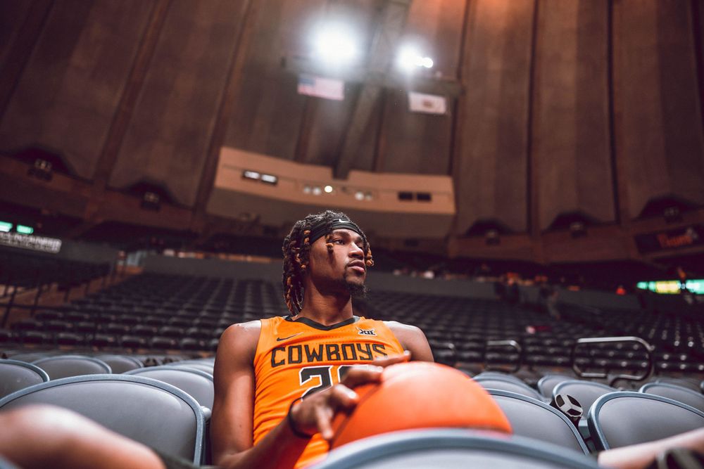 Orange-uniformed basketball player rests in stadium seating before game.