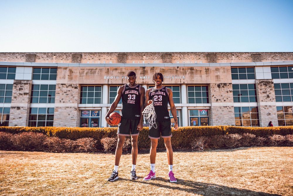 Two Oklahoma State basketball players standing in front of campus building.