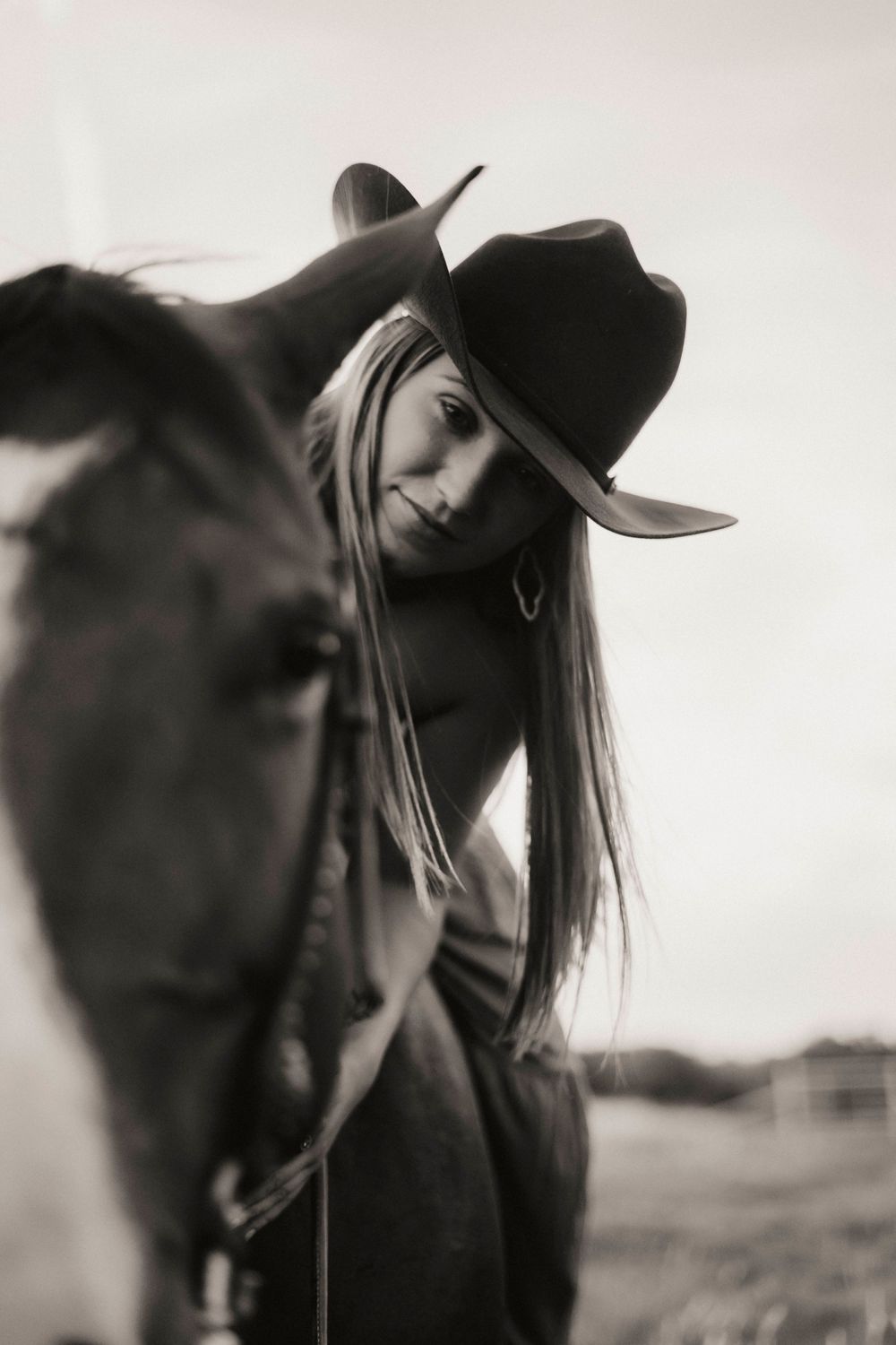 An artistic black and white close-up of a horse and rider wearing a western hat.