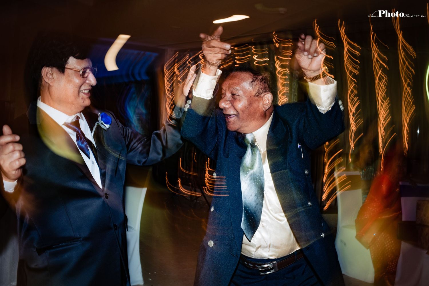 Two men in suits dancing and celebrating with raised arms in a dimly lit venue.
