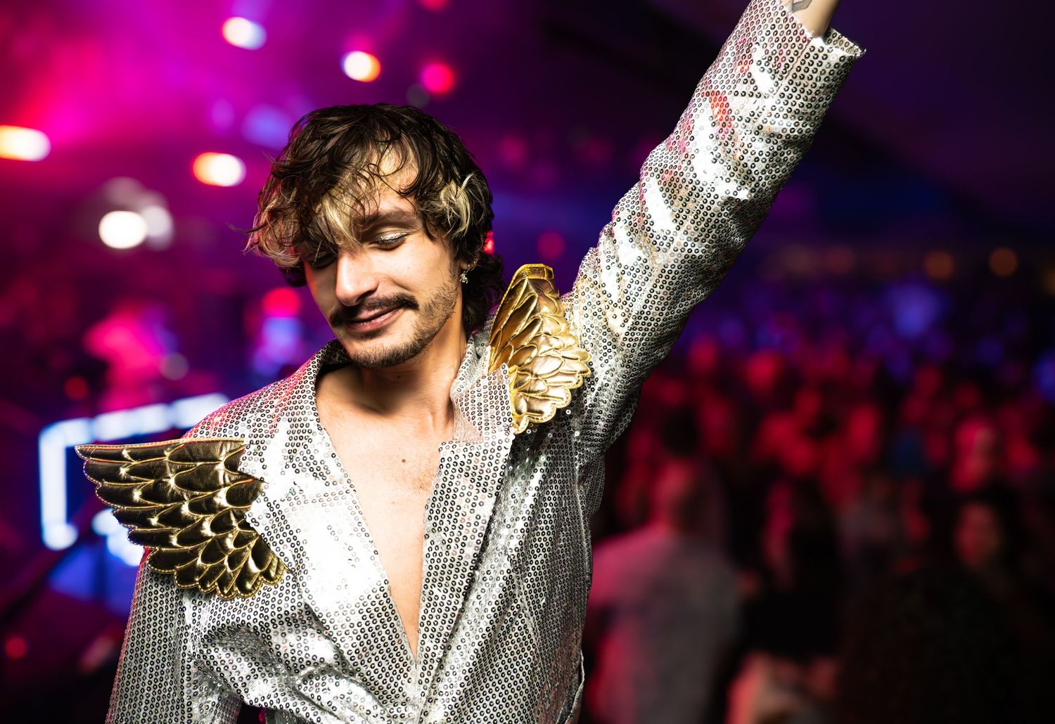 Performer in sparkly silver outfit on stage with dramatic lighting.