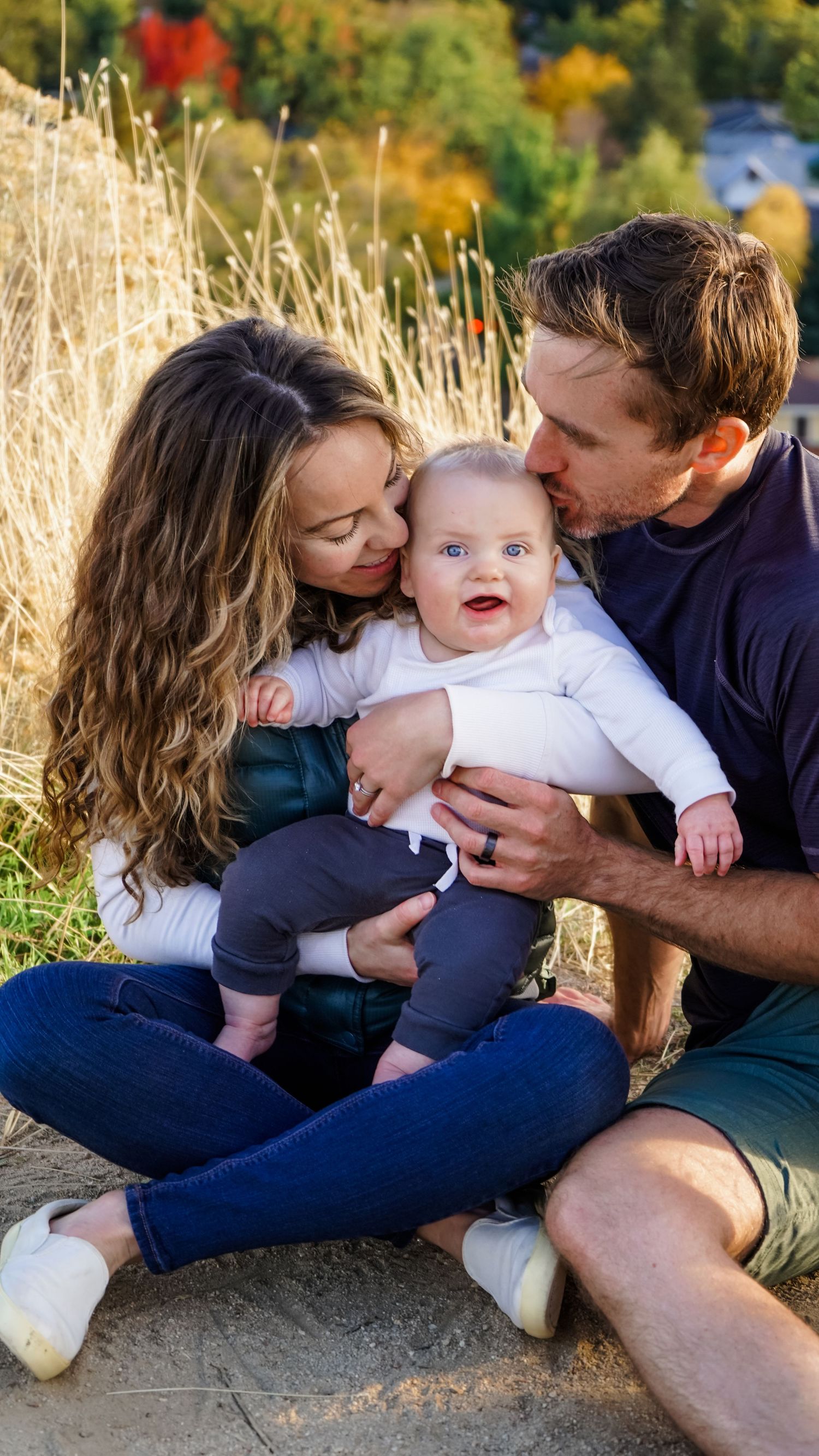 A young family shares tender moments together against a backdrop of autumn foliage.