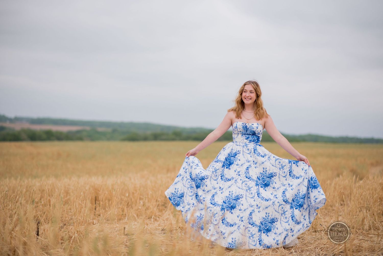 Woman in a blue floral ballgown twirls joyfully in a rustic wheat field.