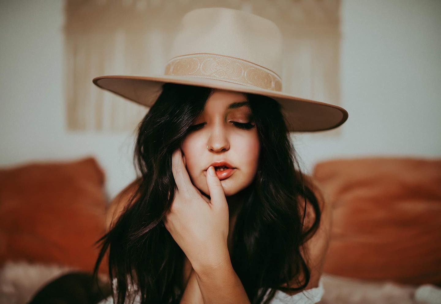Artistic portrait of someone wearing a wide-brimmed hat with finger touching red lips.