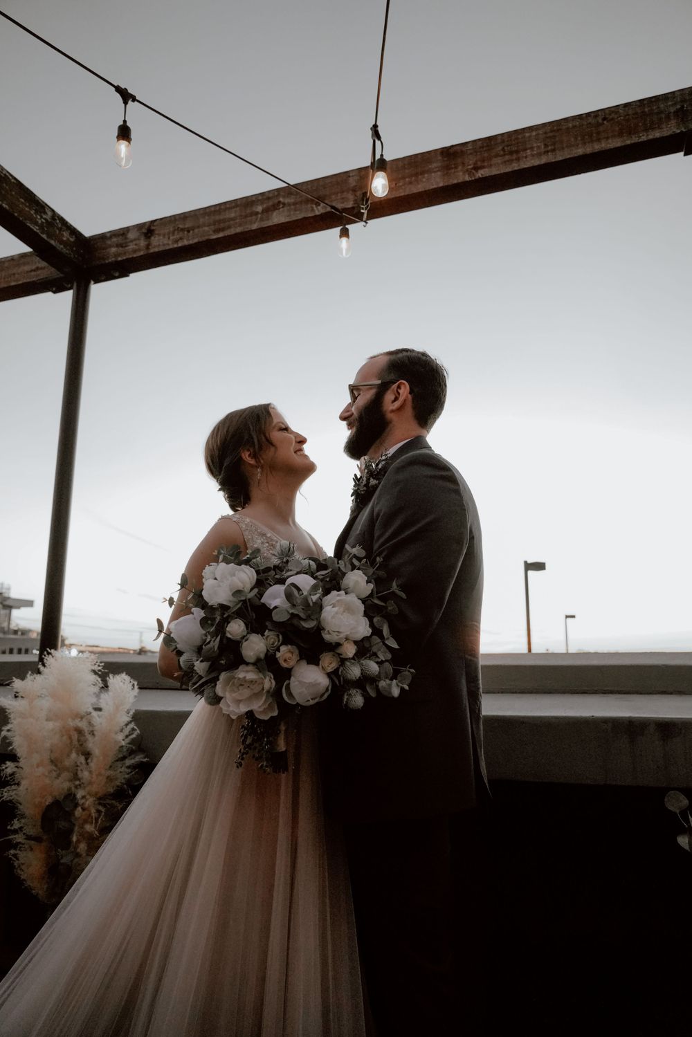 Newlyweds share an intimate moment during their first dance in a rustic venue with wooden beams and string lights.