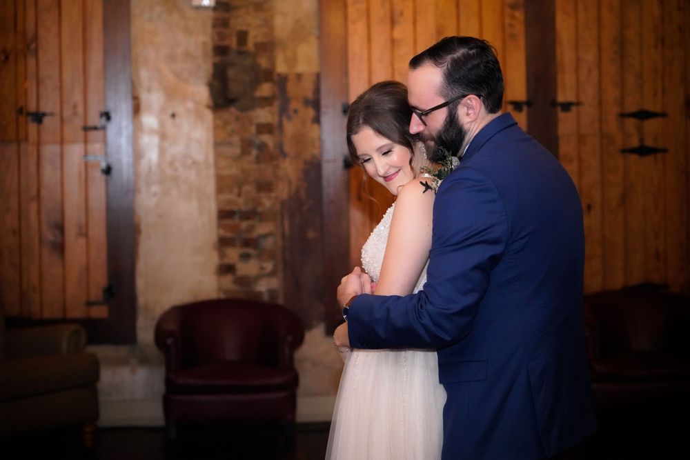 Wedding couple shares a romantic dance under warm lighting in a rustic indoor venue.