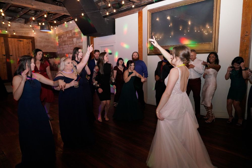 Wedding guests dancing and celebrating at a lively reception with string lights overhead.