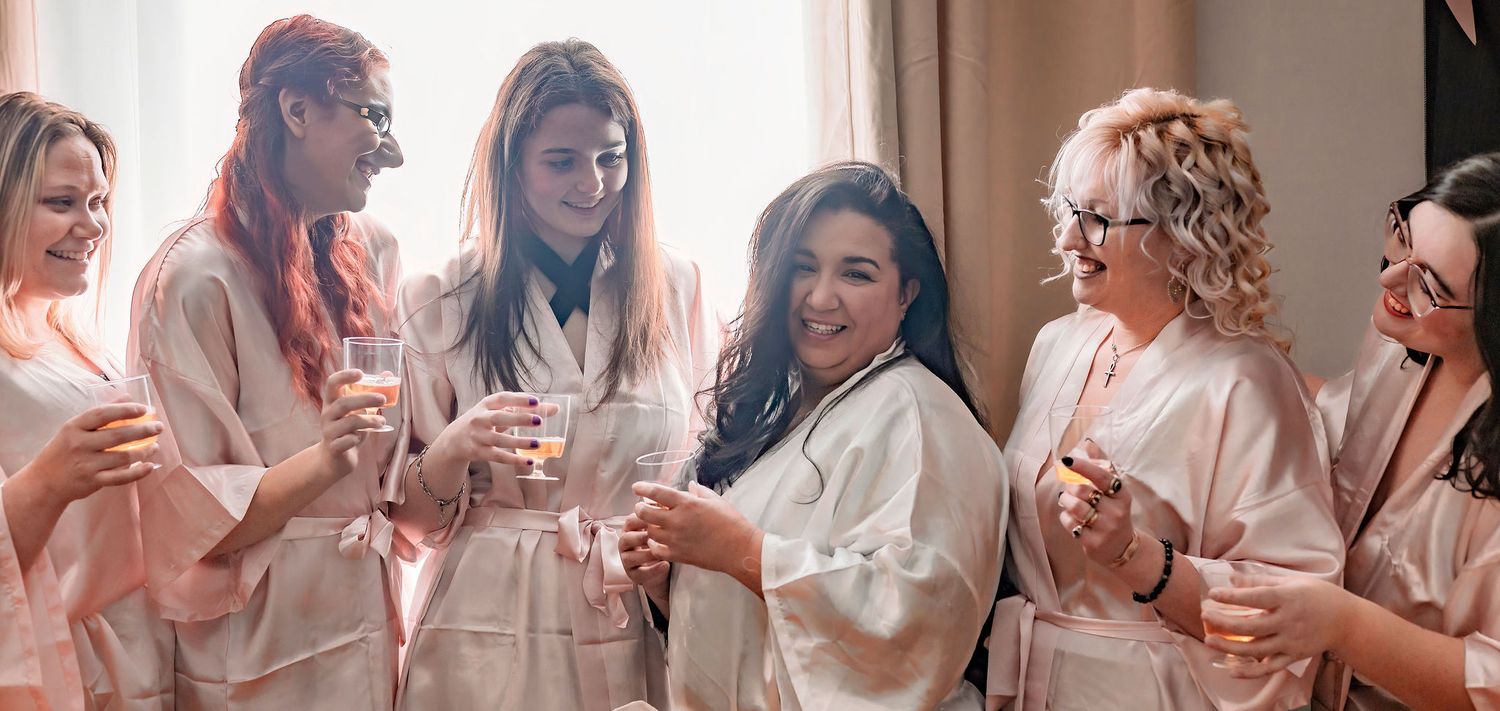 Friends in robes enjoying drinks and laughter at casual indoor celebration.