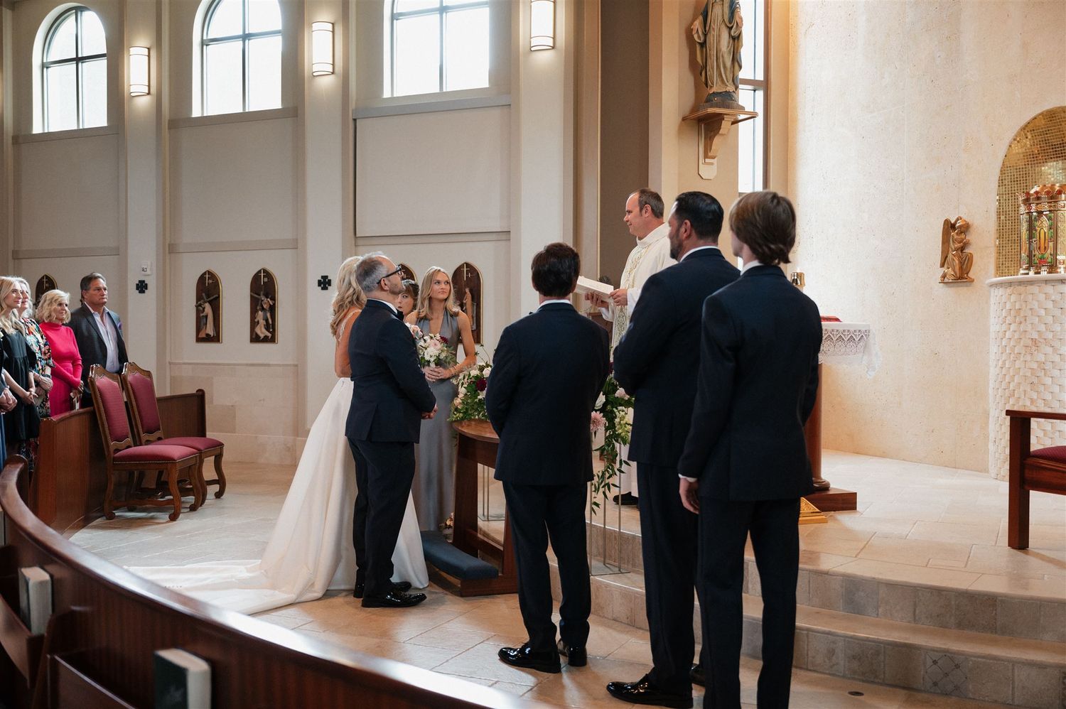 Wedding ceremony at church altar with wedding party and priest.