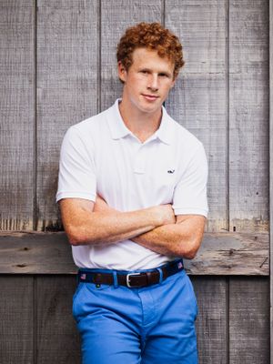 senior boy in blue shorts leaning on barn