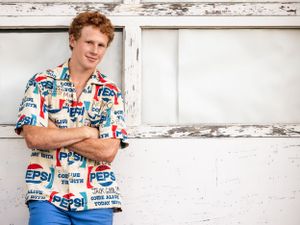 senior boy in Pepsi shirt leaning on white garage with arms folded