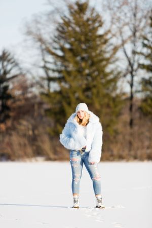 high school senior in blue fur coat standing on ice on sunny day