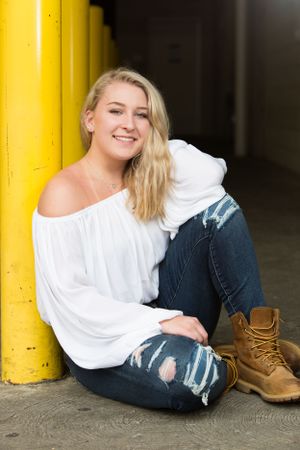 senior girl leaning on yellow pylon with ripped jeans and white shirt