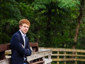 high school boy in suite leaning on bridge