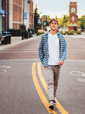 senior boy walking down center yellow lines of street with clocktower behind