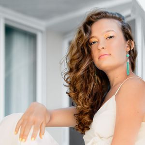 girl with long dark hair in white jump suite on stairs looking down
