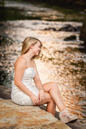 high school senior girl in white dress by golden water swinging hair
