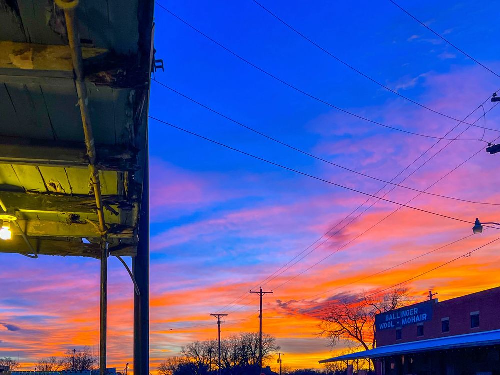 Vibrant pink and orange sunset sky with power lines and urban structures in foreground.