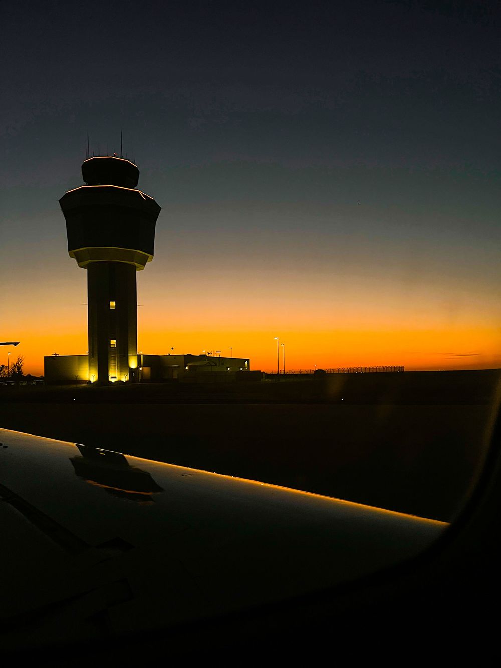 Silhouette of airport control tower against vibrant orange sunset sky.