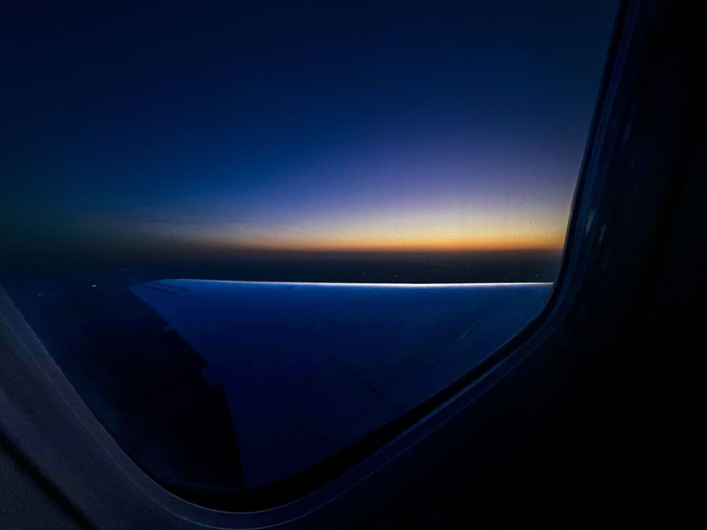 View of sunset sky from airplane window showing dark blue and orange horizon.