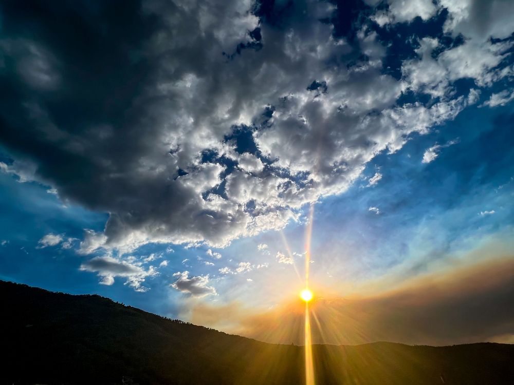 Sunset rays pierce through dramatic clouds over mountain silhouette.