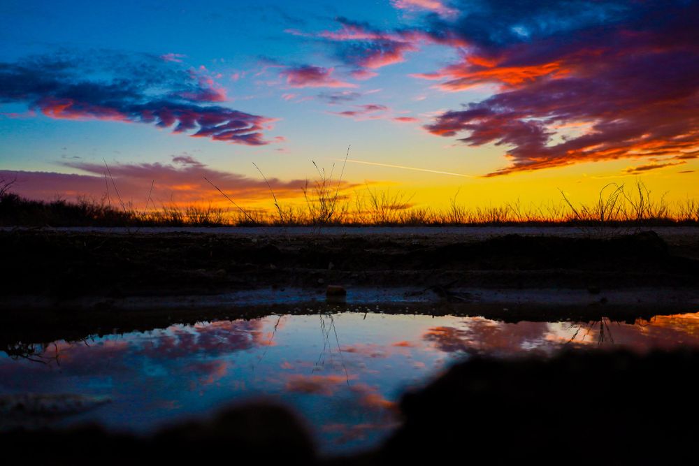 Vibrant sunset reflects in still water with colorful clouds and gradient sky.