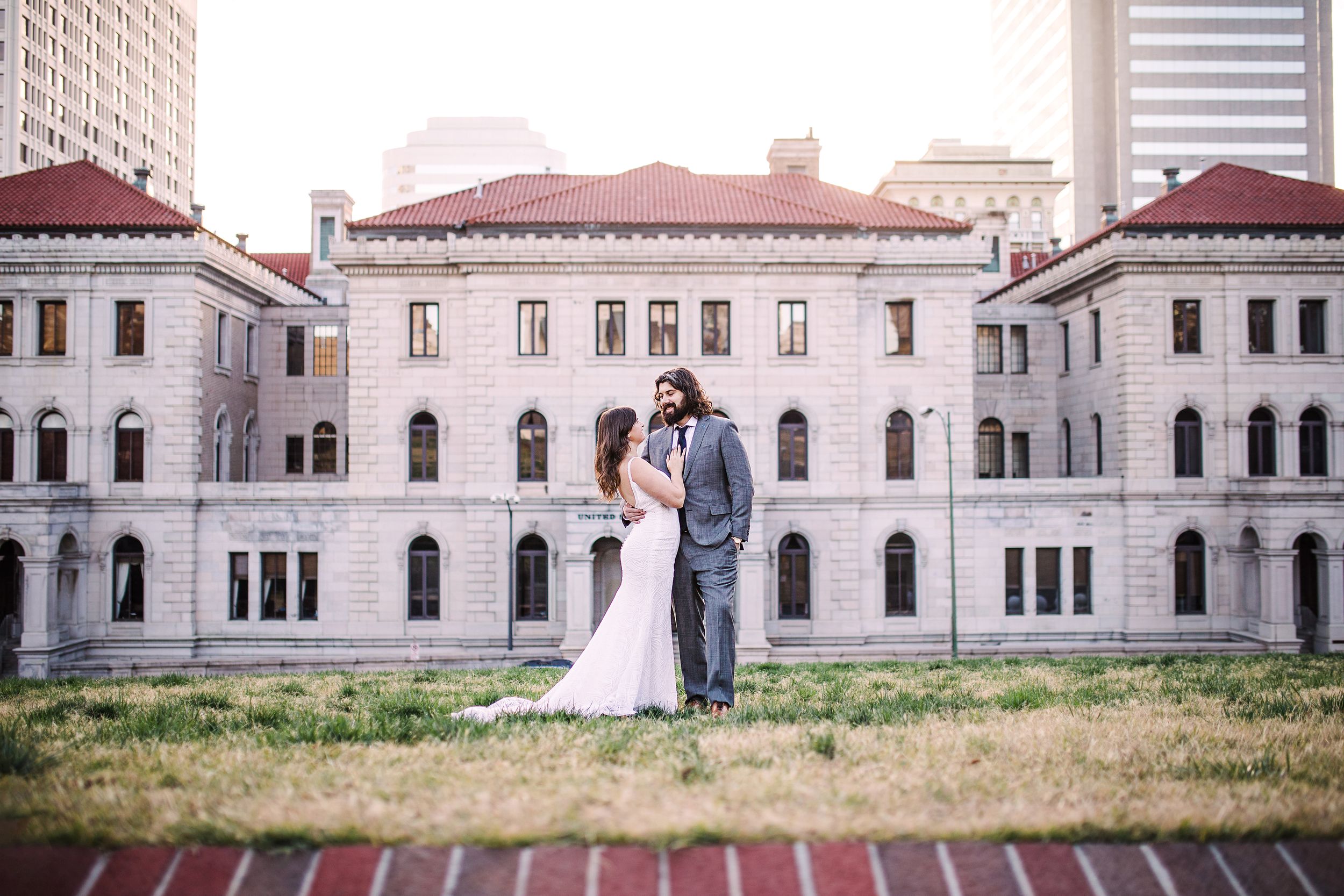 Bride and groom posing in front of historic stone building in downtown urban setting.