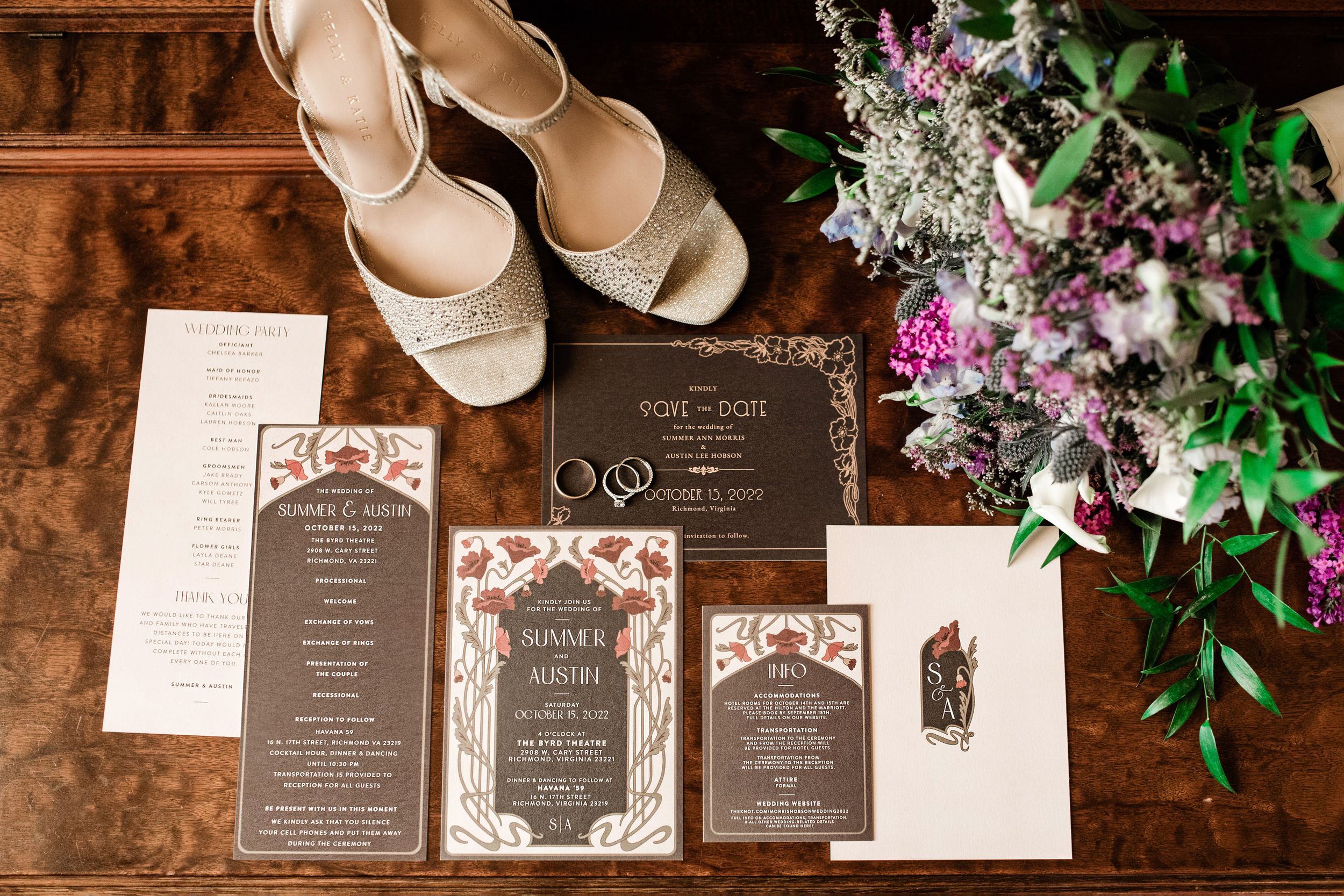 Wedding flat lay with invitations, rings, bridal shoes, and purple floral bouquet on wood table.