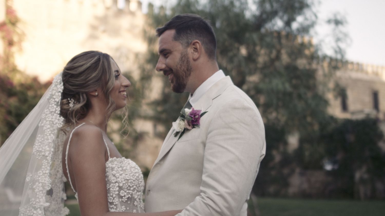 Romantic wedding portrait with couple in white attire against sunset garden backdrop.