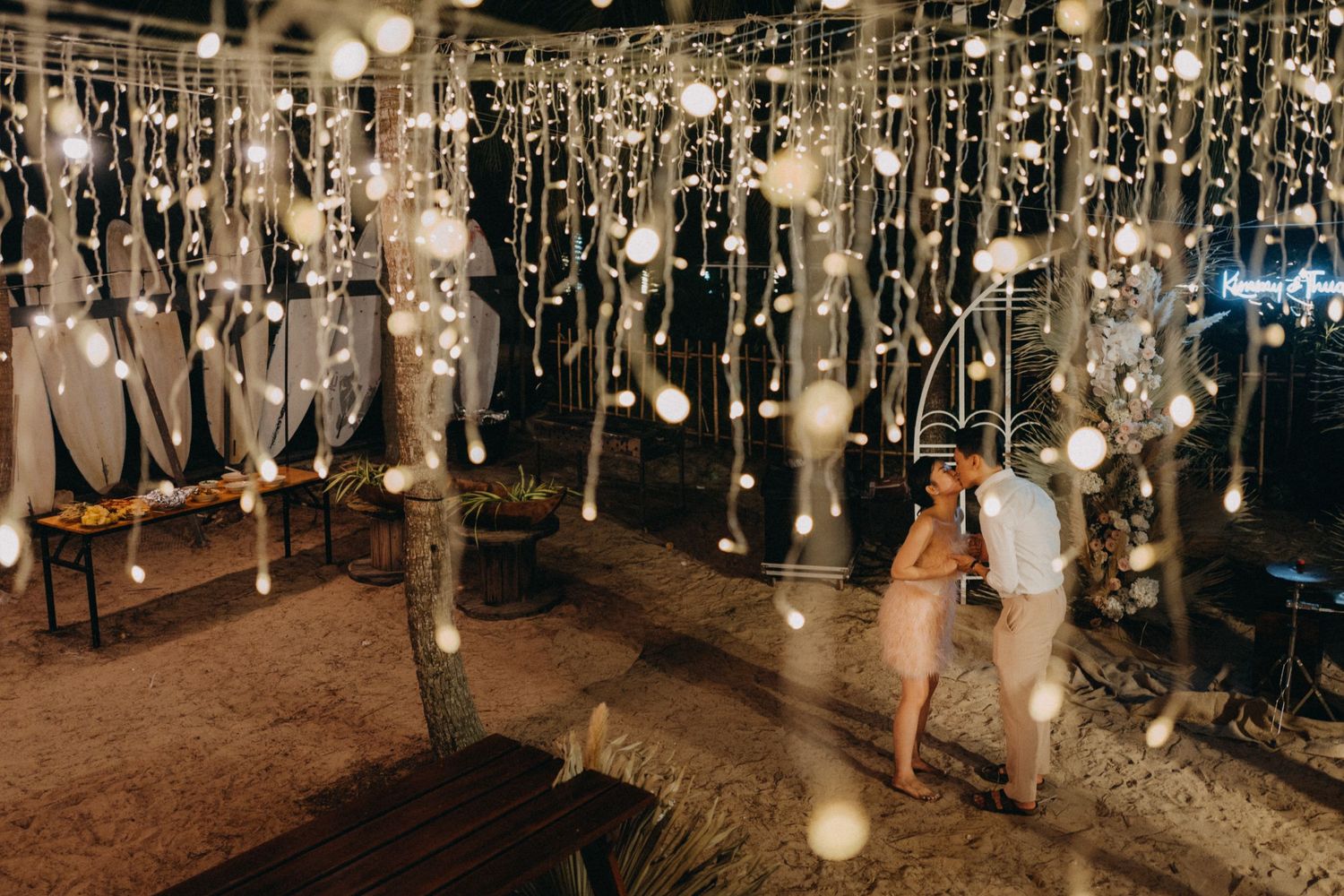 Couple sharing a romantic moment under thousands of hanging fairy lights at an elegant outdoor wedding venue.