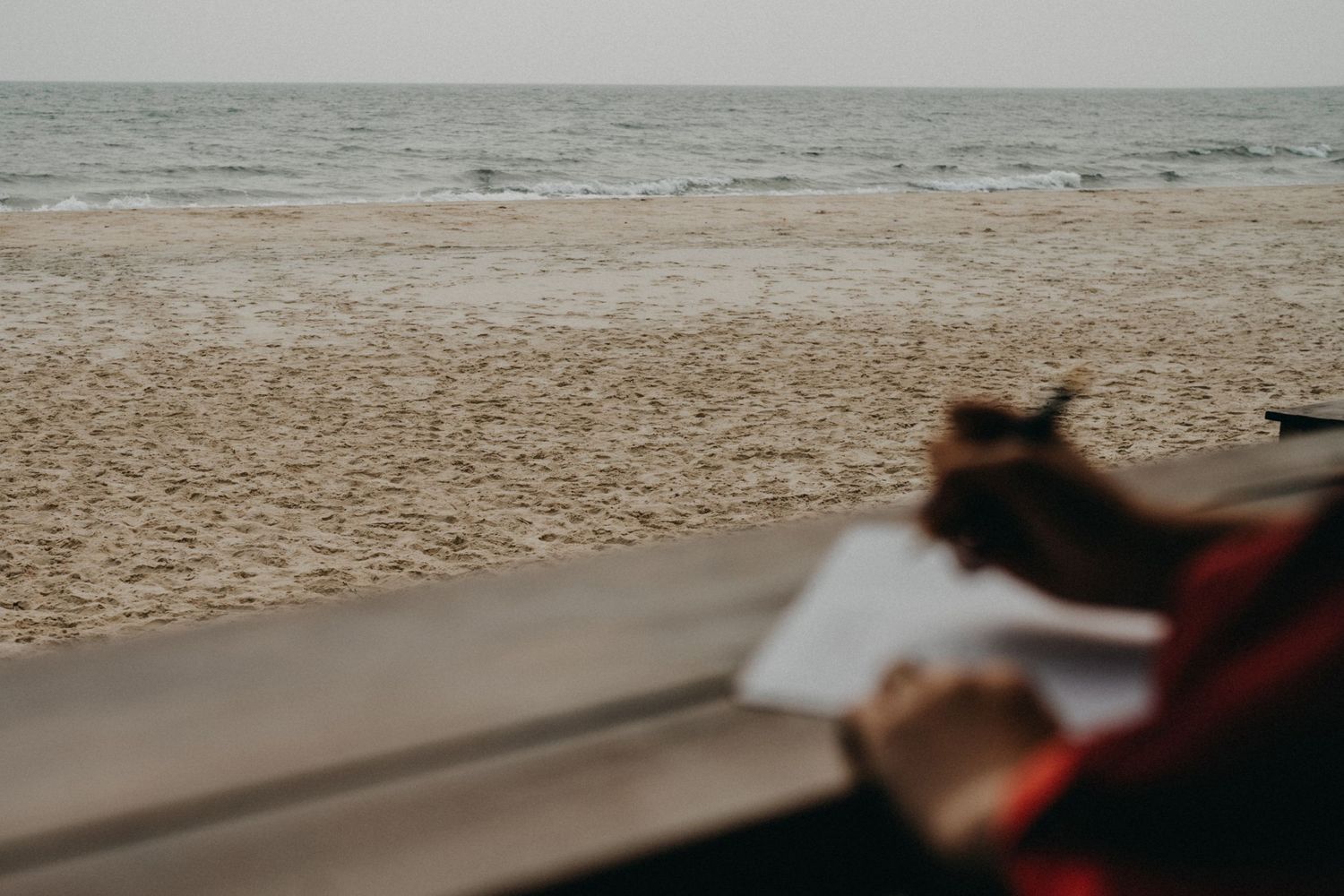 Blurred silhouette of person writing wedding vows overlooking a serene sandy ocean beach.