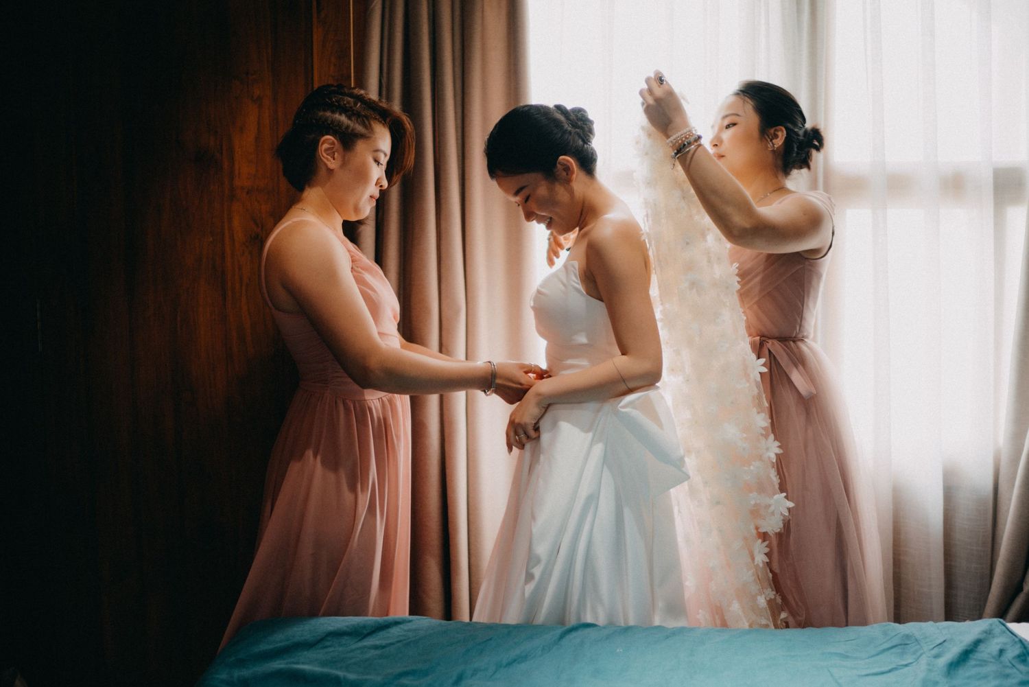 Bridesmaids in pink dresses helping bride with wedding gown and veil.