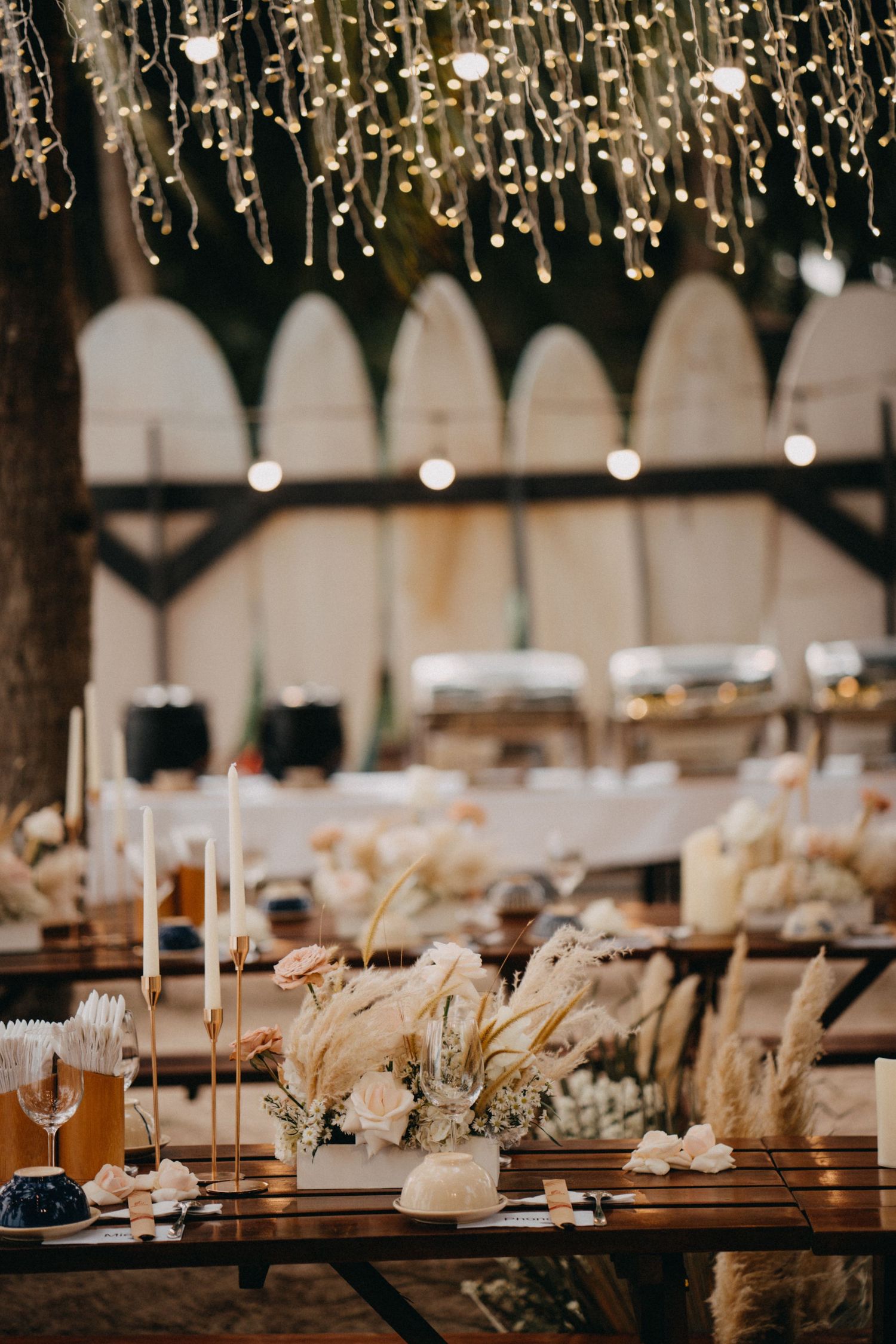 Romantic boho wedding reception with fairy lights, candles, and pampas grass.