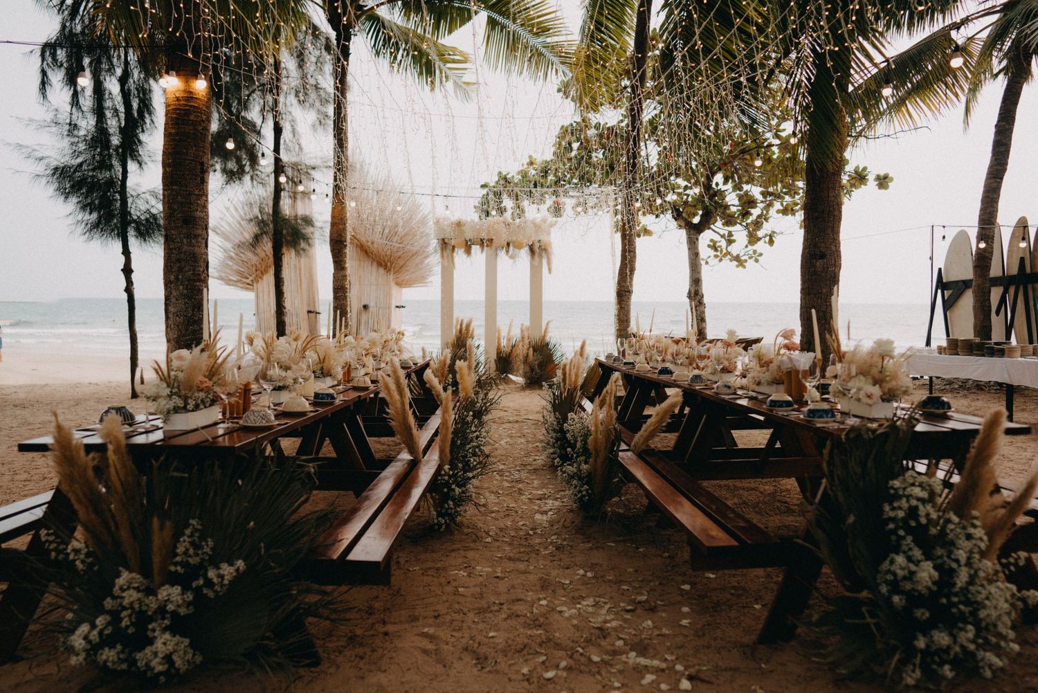 Stunning beachside boho wedding reception setup with palm trees and fairy lights.