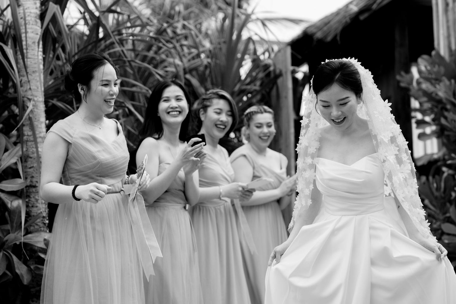 Bride and bridesmaids laughing together in black and white outdoor wedding photo.