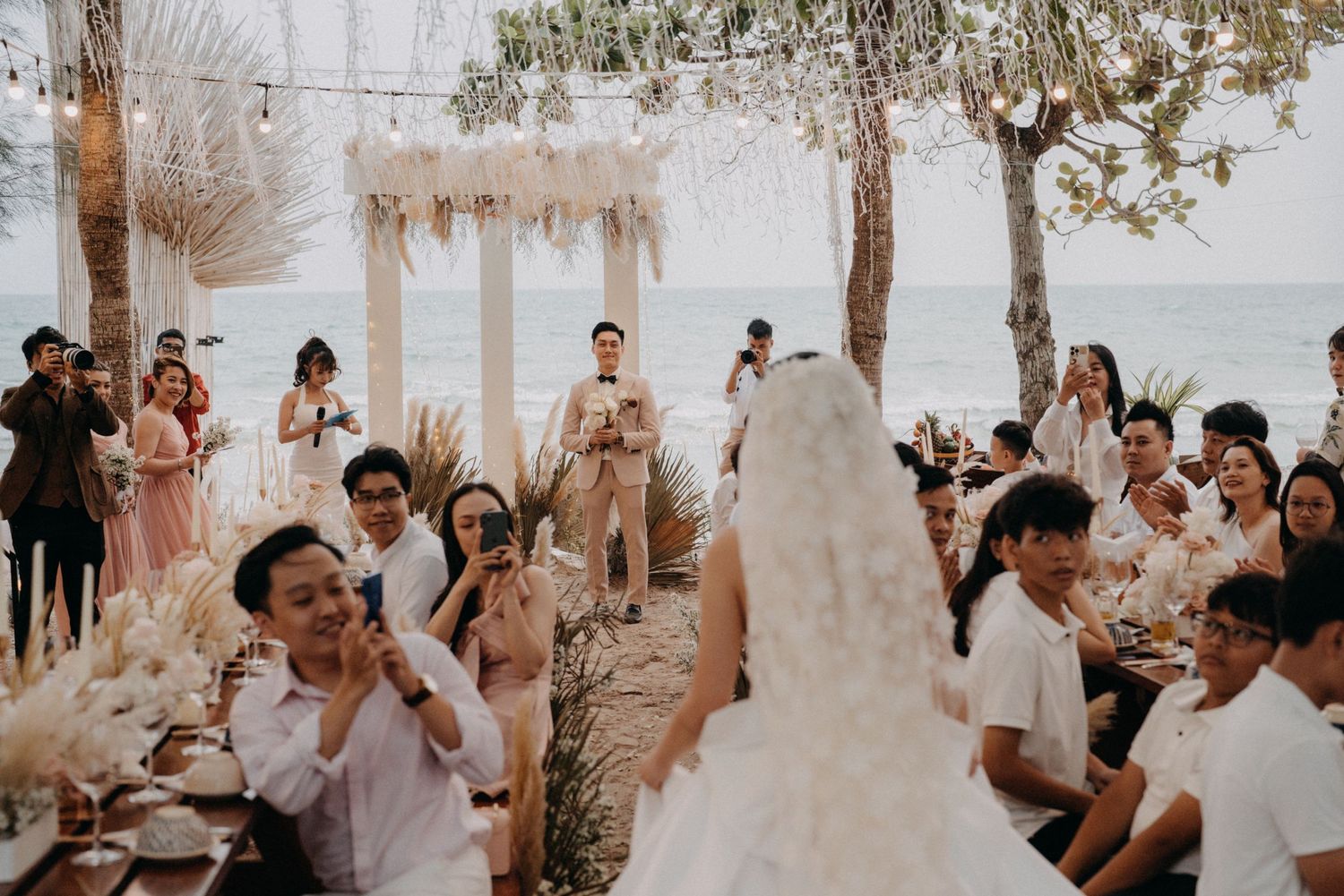 Bride and groom walk through cheering guests at a boho beach wedding reception by the ocean.