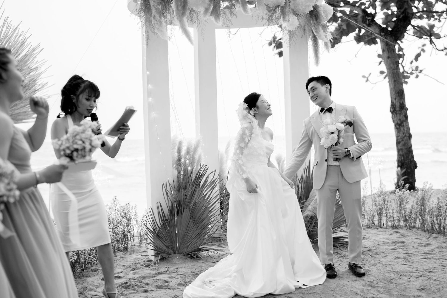 Bride and groom smile joyfully during their beachside wedding ceremony in black and white photo.