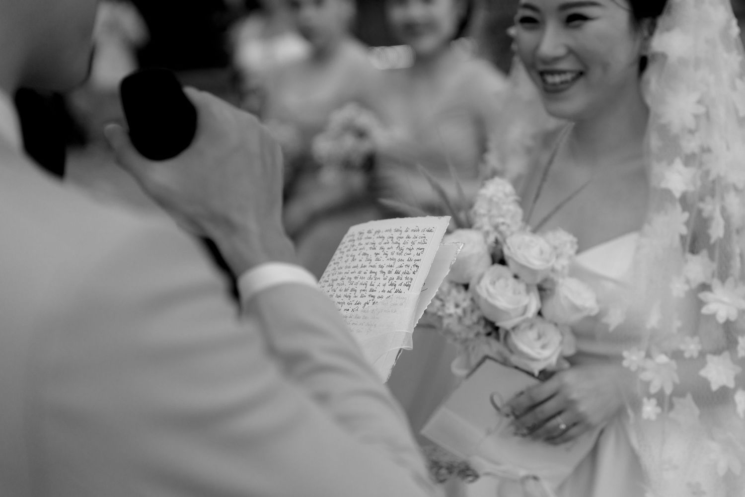 Smiling bride holds a white bouquet as someone reads from a book during the wedding ceremony.