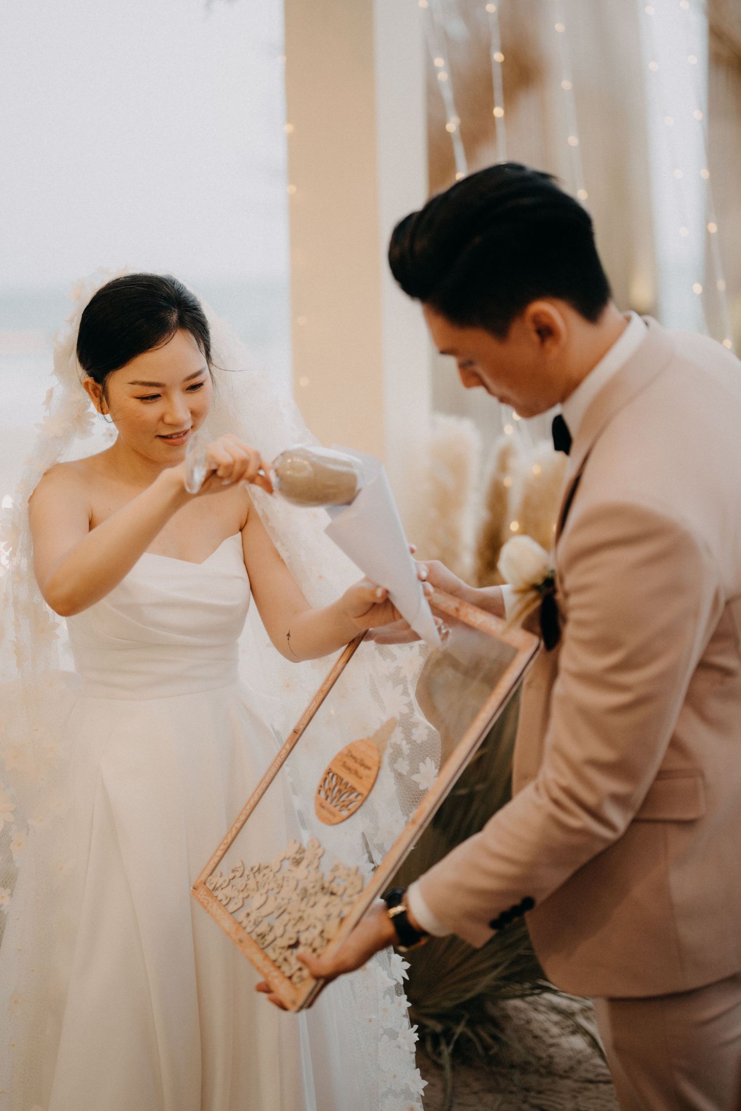 Bride pours sand into a wooden shadow box held by groom during a wedding unity ceremony.