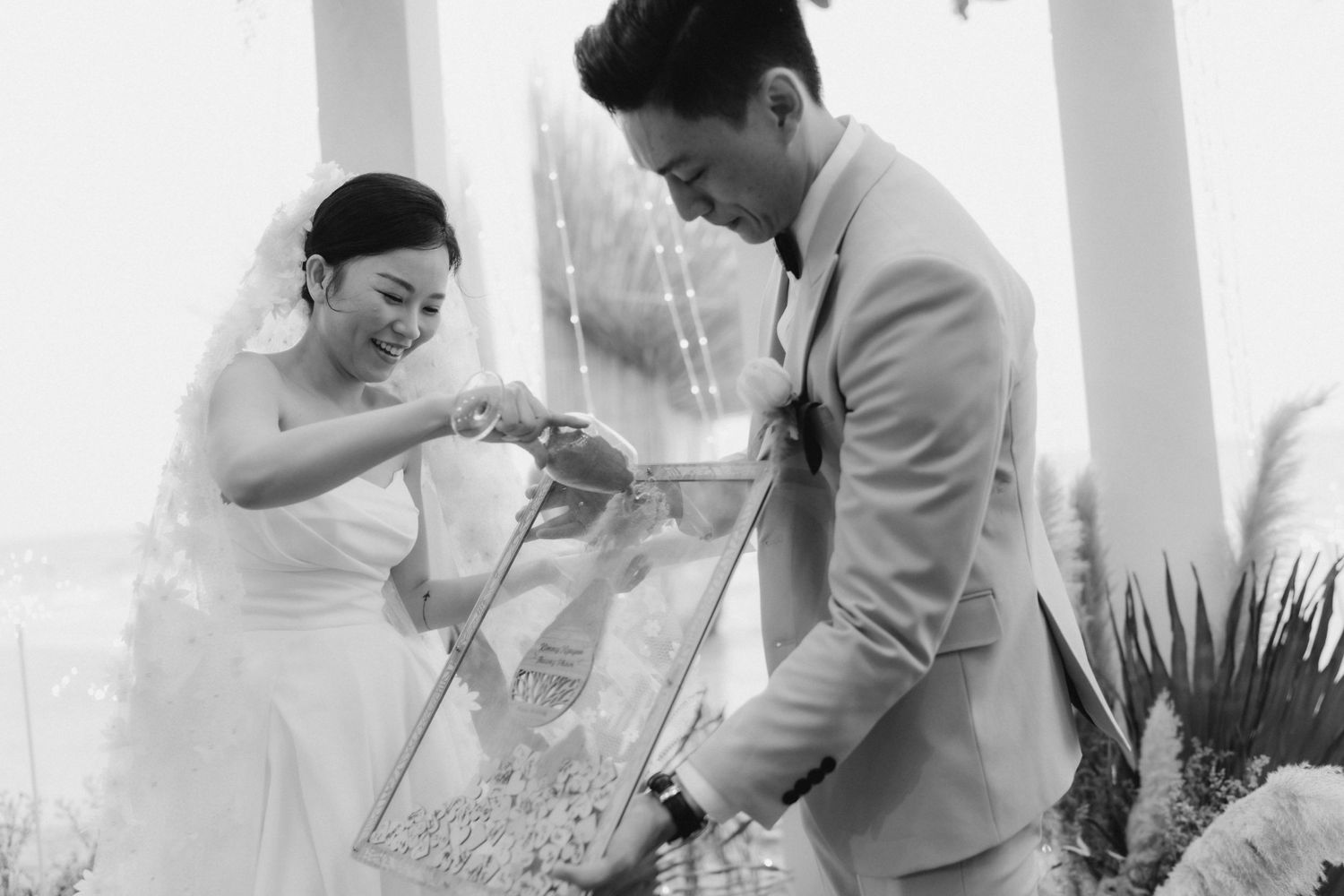 Black and white photo of bride and groom performing a unity sand ceremony at the altar.