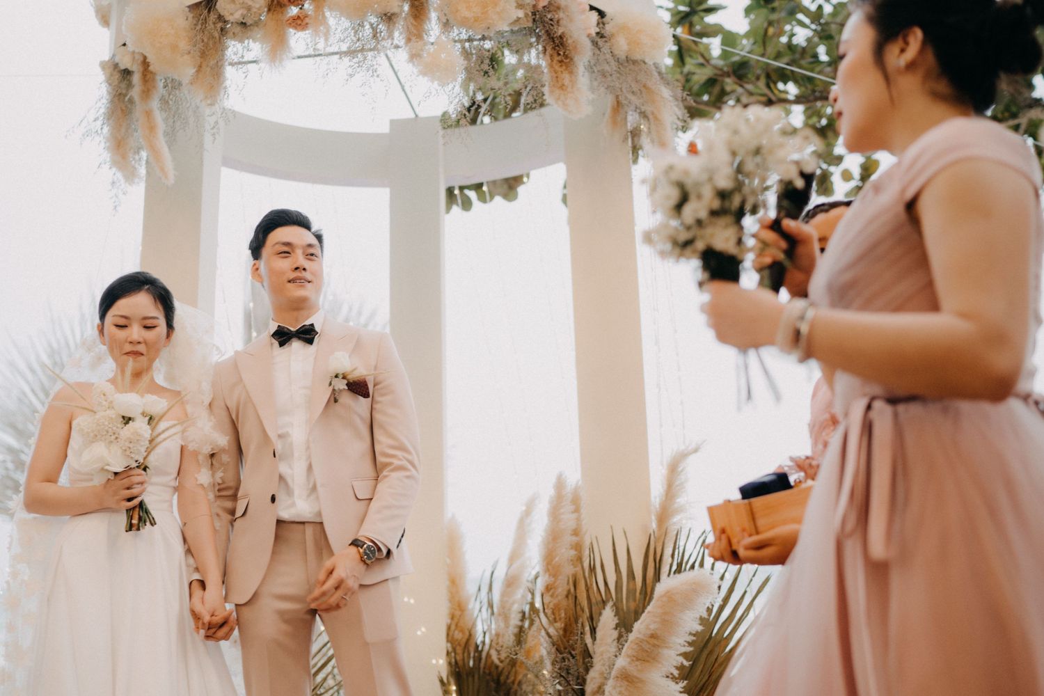 Bride and groom stand at ceremony altar while bridesmaid reads speech at beach wedding.