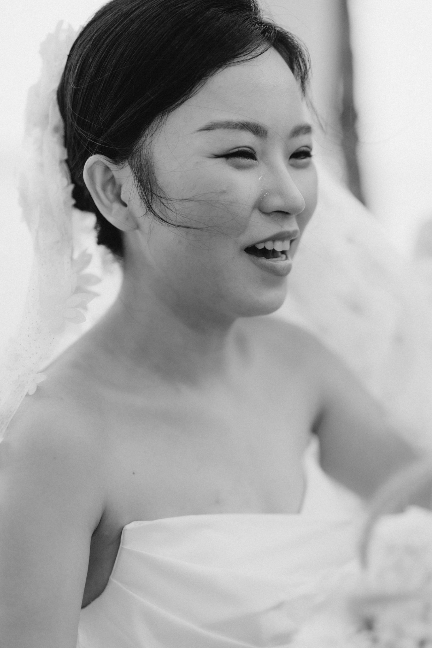 Smiling bride in strapless gown with veil captured in elegant black and white wedding portrait.